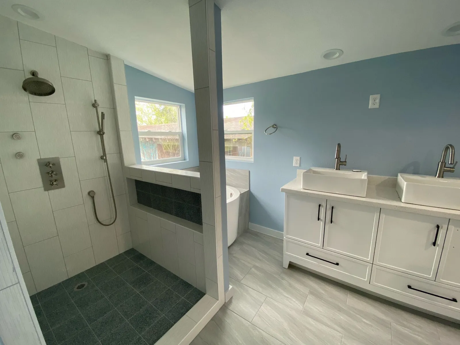 Remodeled primary bathroom with walk-in tile shower, double vessel-sink vanity, and freestanding tub by Detail Construction