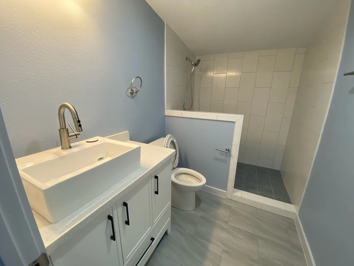 Remodeled bathroom with white vessel-sink vanity, walk-in tile shower with half wall, and gray tile flooring