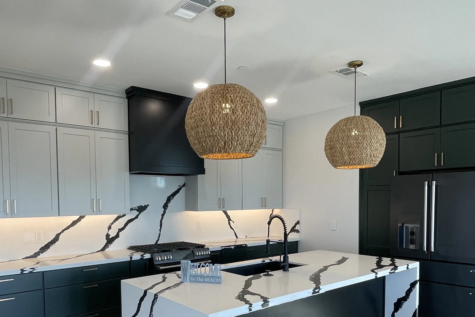 Remodeled kitchen with black shaker cabinets, waterfall quartz island, and woven pendant lights by Detail Construction