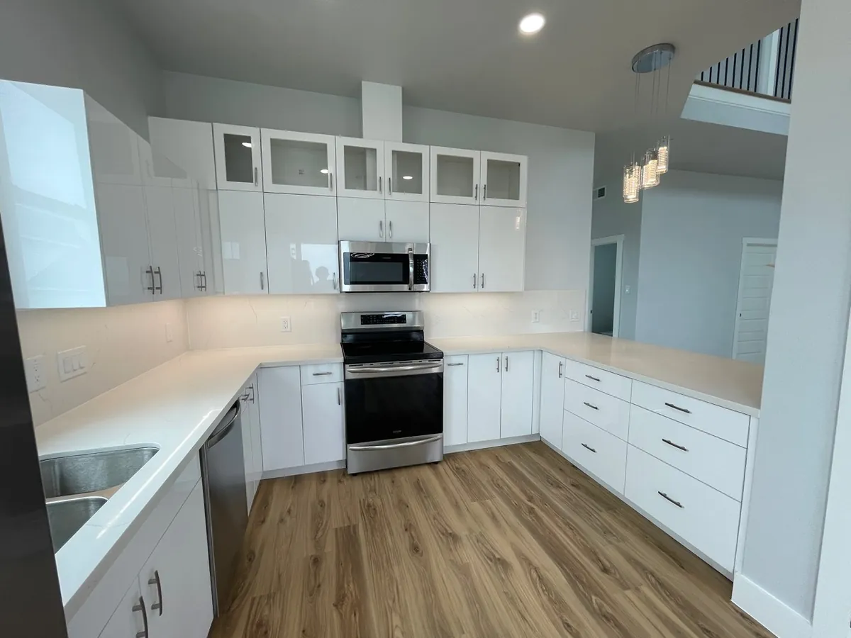 Bright white U-shaped kitchen remodel with quartz countertops, stainless appliances, and wood-look flooring