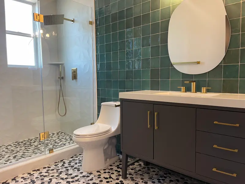 Green tile walk-in shower beside a navy vanity with brass fixtures