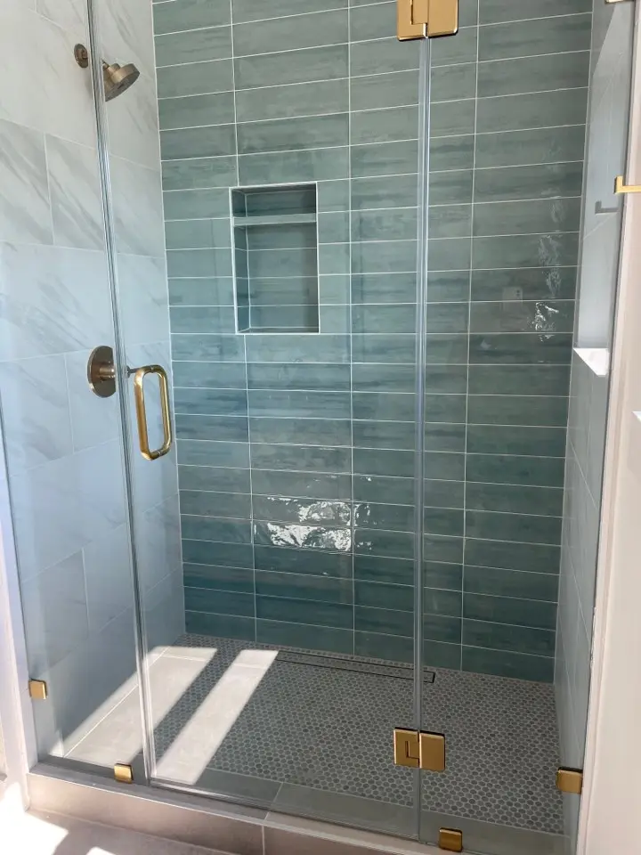 Green glazed tile walk-in shower with frameless glass and brass hardware