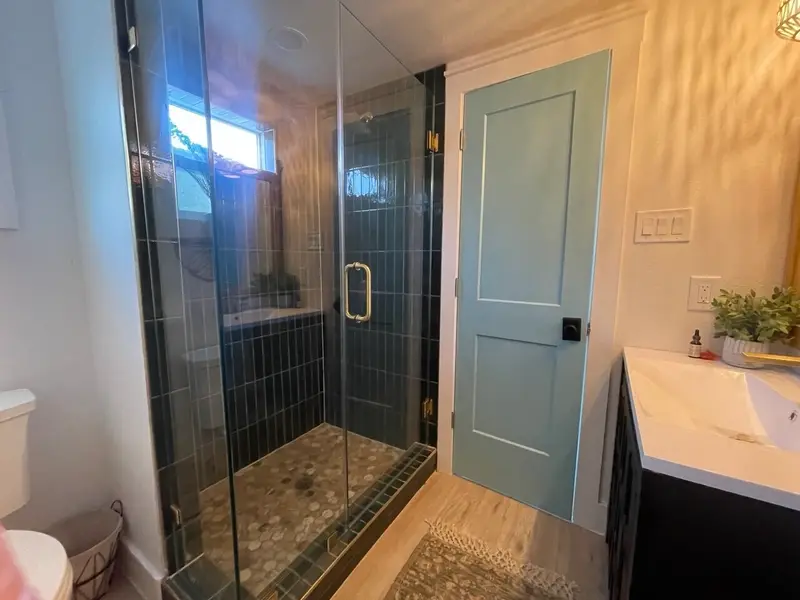 Dark tile walk-in shower with pebble floor and frameless glass door