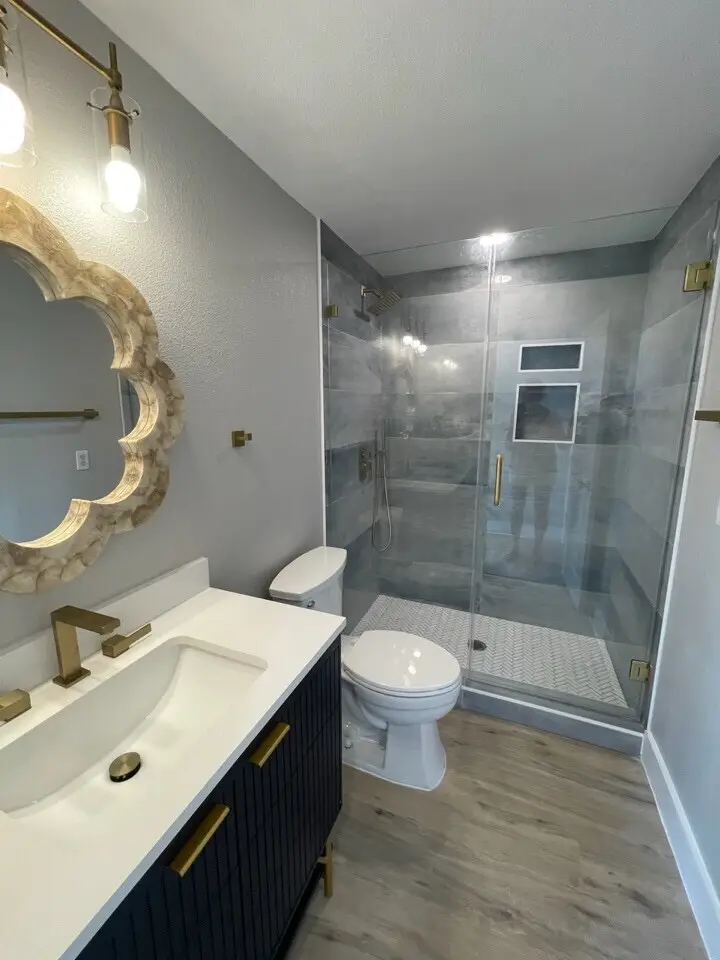 Glass-enclosed shower with ornate gold mirror and white vanity