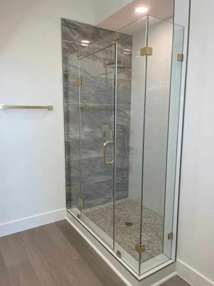 Frameless glass corner shower with marble-look tile and brass hardware