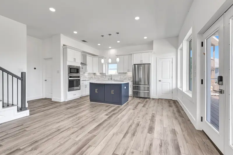 Open-concept kitchen remodel with navy island, white shaker cabinets, and wood-look plank flooring