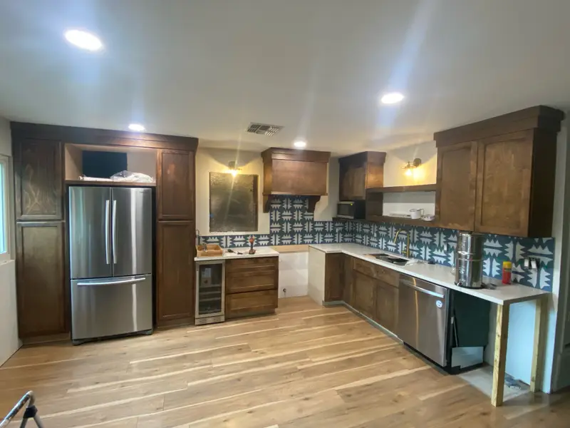 L-shaped kitchen with stained wood cabinets, patterned tile backsplash, and stainless appliances
