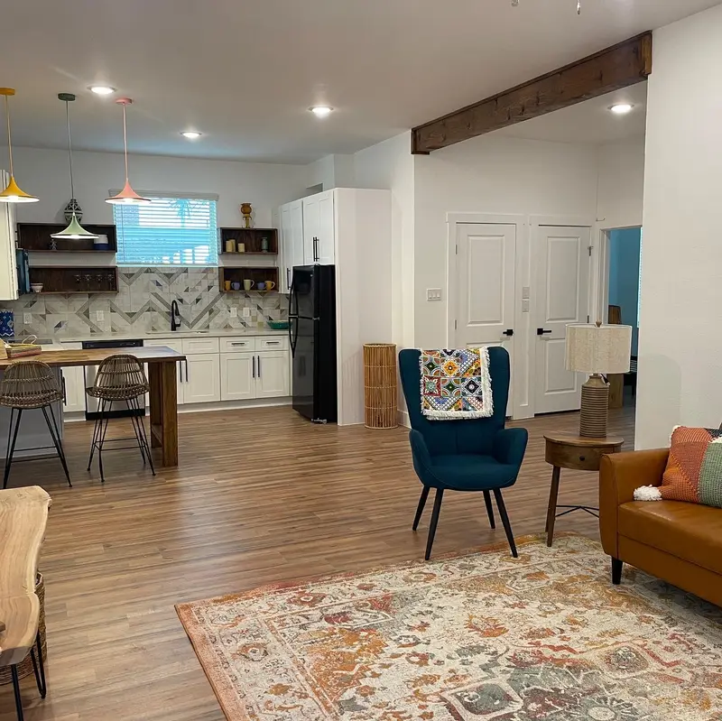 Open kitchen and living area with white cabinets, patterned backsplash, and wood-look floors