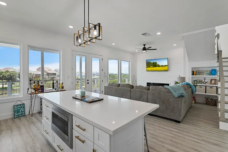 White kitchen island with quartz top and pendant light opening to the living room